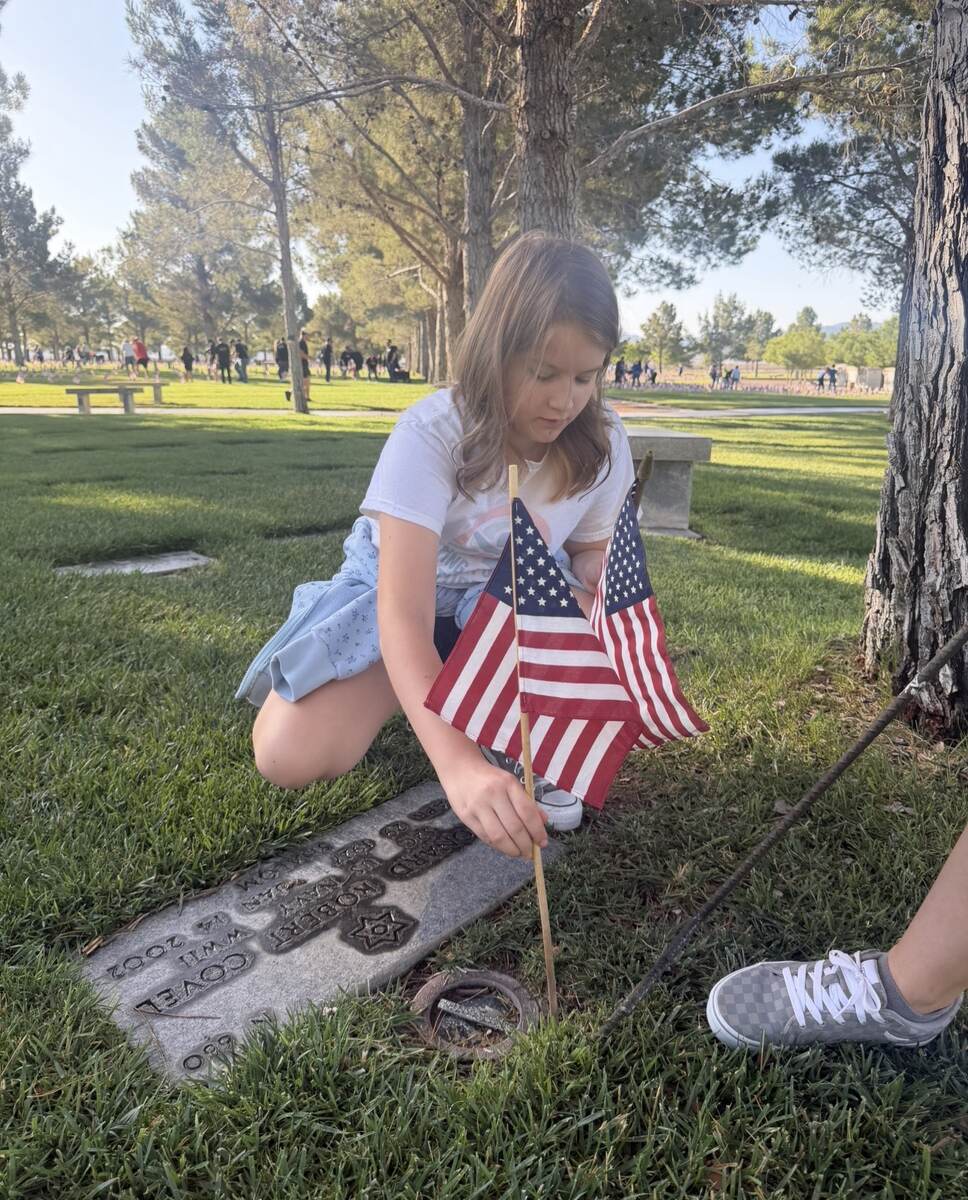 Young girl placing an American flag at a veteran's memorial marker